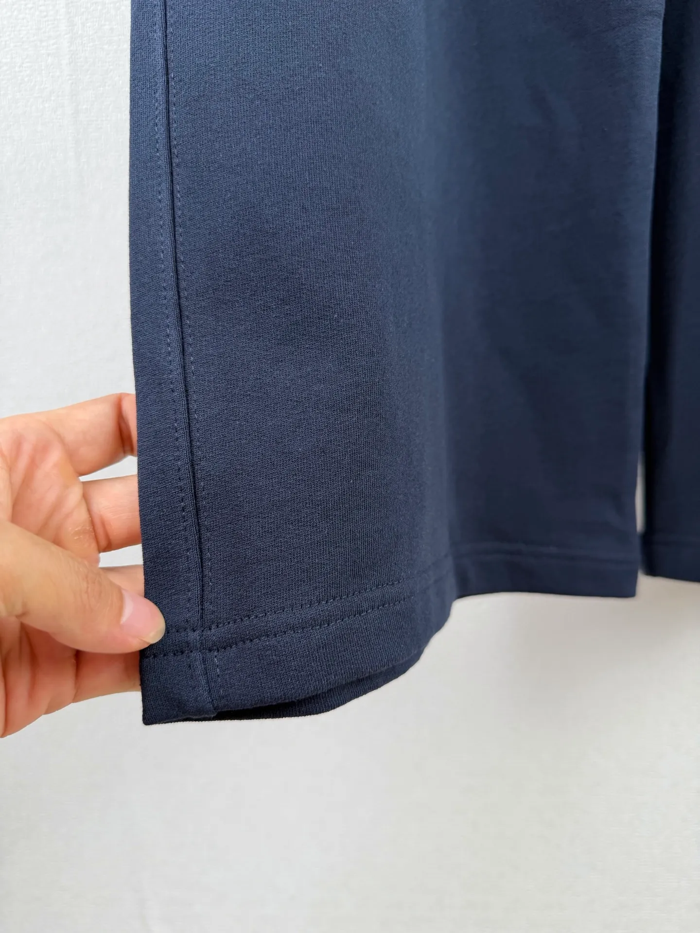 ACNE STUDIOS embroidered logo fleece sweatpants wide-leg trousers. Fabric: 32-count double yarn top + 16-count terry bottom yarn G The veil is made of 32-count fine yarn. The high-count yarn is smooth and delicate. After weaving, it forms a smooth and compact surface. It not only resists pilling and wear-resistant, but also gives the fabric a touch as delicate as skin. The base yarn is made of 16-count roving. The low-count yarn is fluffy and hairy. It naturally forms a rich terry layer during the weaving process, providing a sufficient source of fiber for subsequent sanding. This combination of fine surfaces and thick soles strikes a perfect balance between warmth and skin-friendliness. Mechanical sanding is the soul process of this fabric. By rubbing the bottom surface of the roller wrapped with emery leather at high speed, the fiber ends of the 16-count roving are evenly pulled out and cut off, forming a dense and uniform short pile layer. The smoothness and neatness of needle embroidery and the soft velvet feel of brushed fabrics form a material dialogue between hardness and softness. The embroidery area is smooth and crisp, with sharp lines, like delicate inscriptions carved on a rich suede canvas; while the surrounding brushed fabric presents a soft matte natural texture. The spacing between stitches is consistent and the strength is balanced to ensure that each stitch is placed accurately. This rigorous stitching structure makes the edges of the logo present a sharp and clear outline, and the strokes of the text are full and smooth. Even the curved turning points of the floral fonts can achieve a smooth transition through the connection of tight stitches.